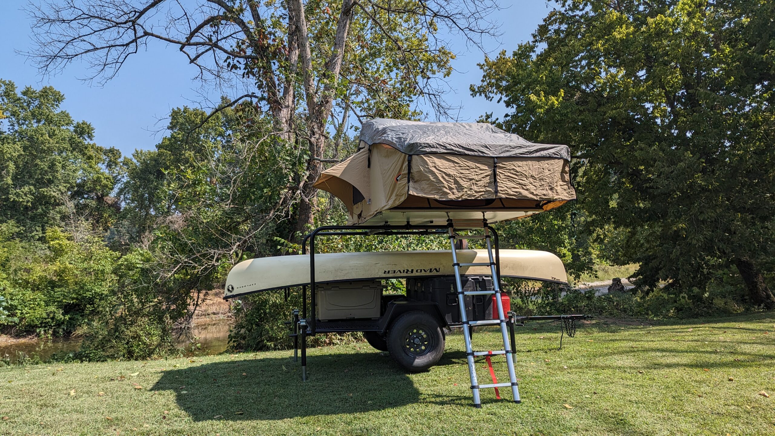 Twain Trailers trailer with Mad River canoe and deployed rooftop tent parked riverside